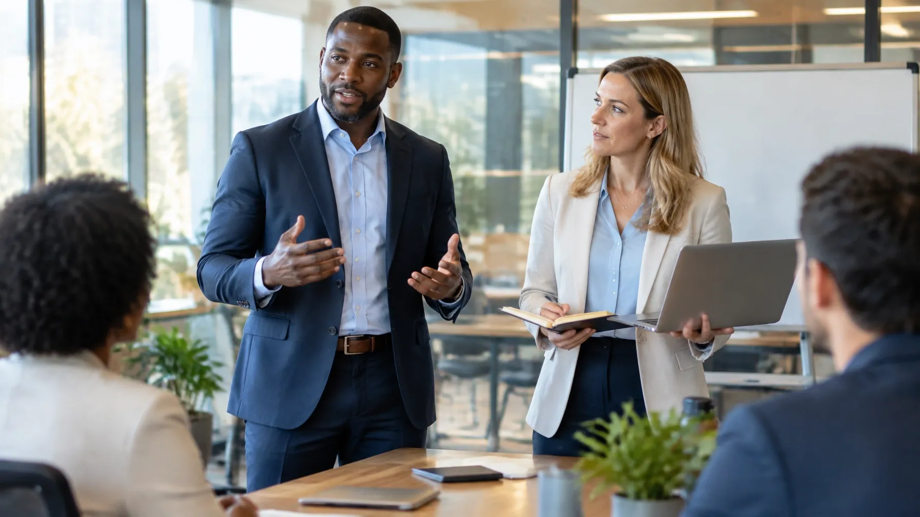 Black man manager leading a strategy briefing with a white woman manager and colleagues in a glass-walled office